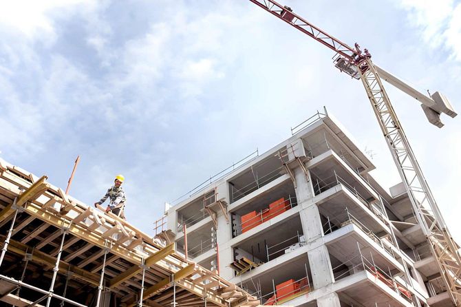 Construction site with partially built concrete building, workers on scaffolding, and a crane overhead
