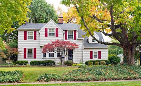 A white house with red shutters and a tree in front of it