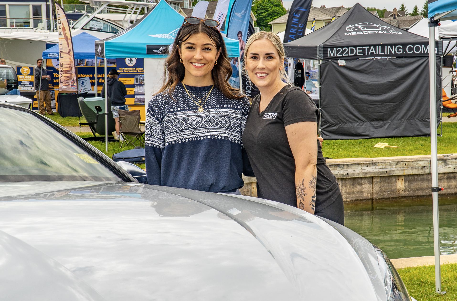 Two women are posing for a picture in front of a car.