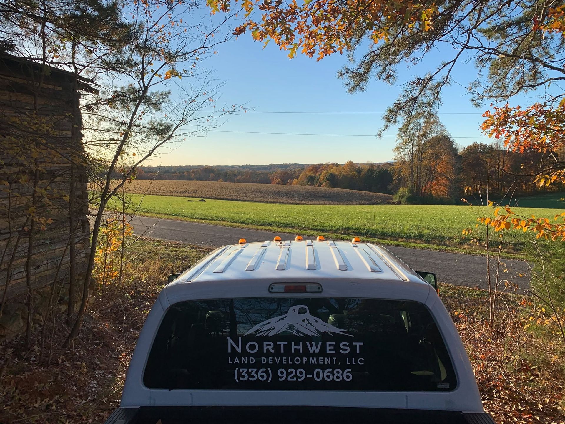 White van by a stone building overlooking a green field and autumn trees at sunset