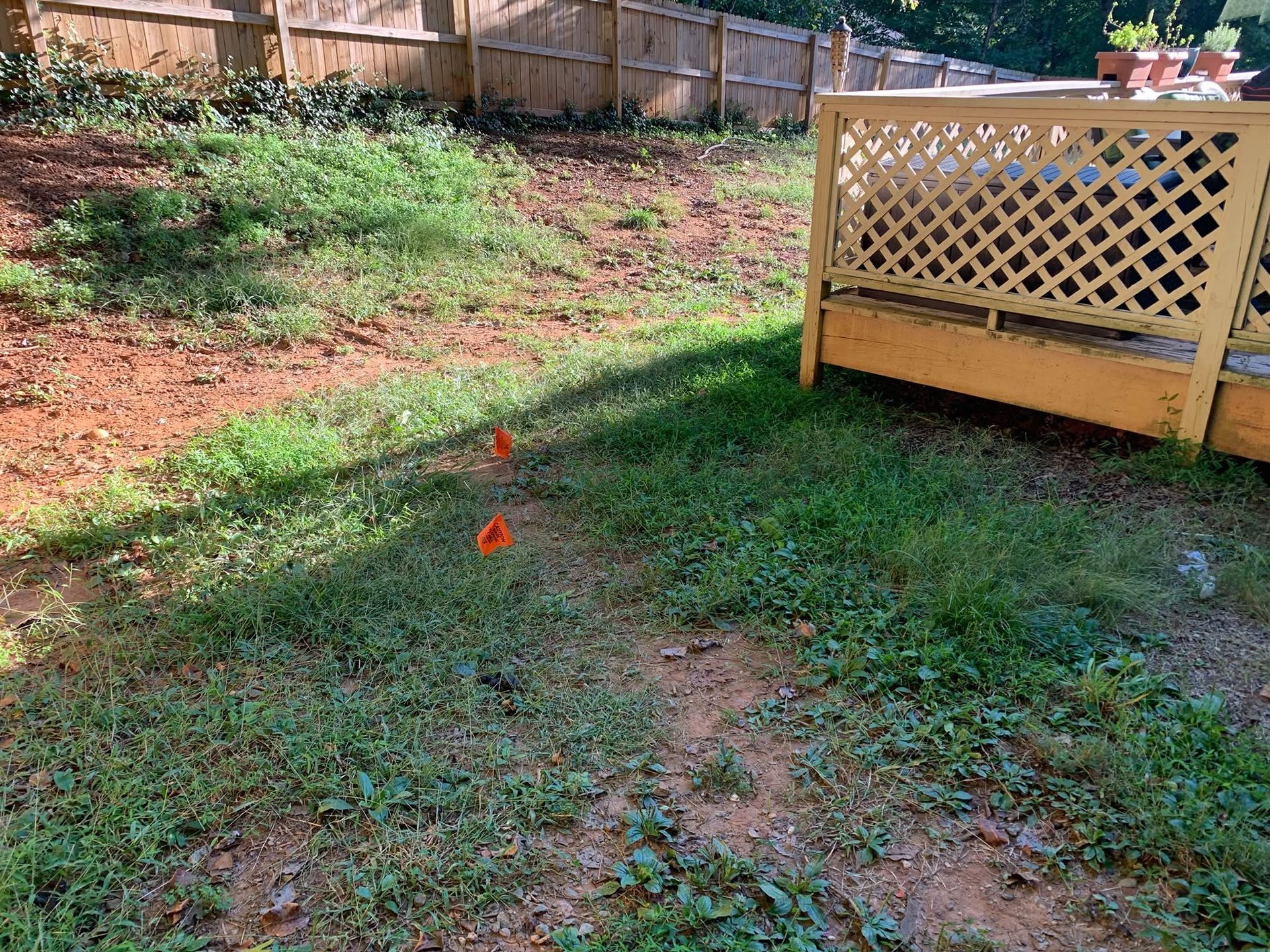 Backyard with grassy slope, two orange flags, and a wooden deck railing on the right.
