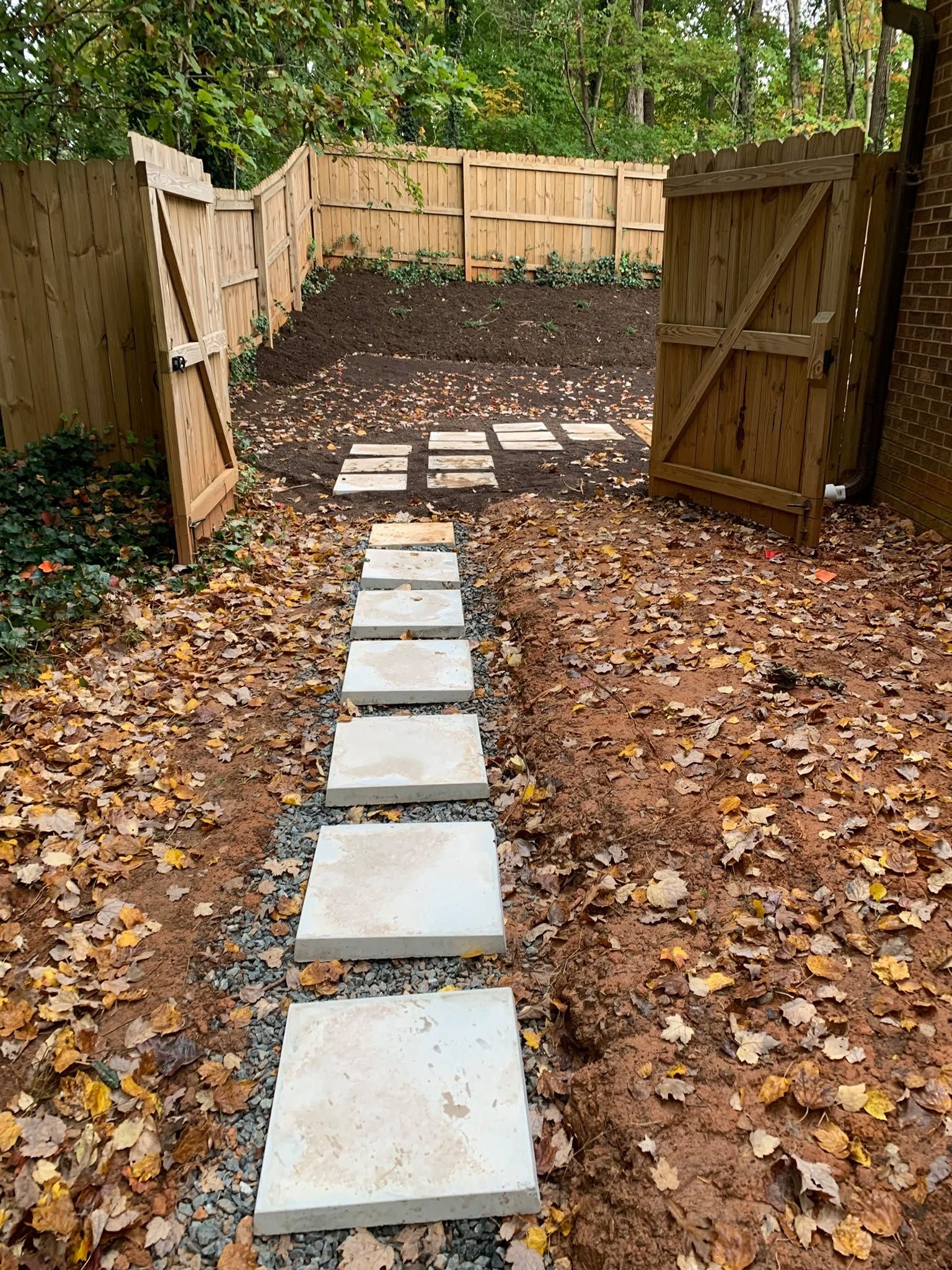 Stepping stones leading through open wooden gates to a leaf-covered yard in the woods