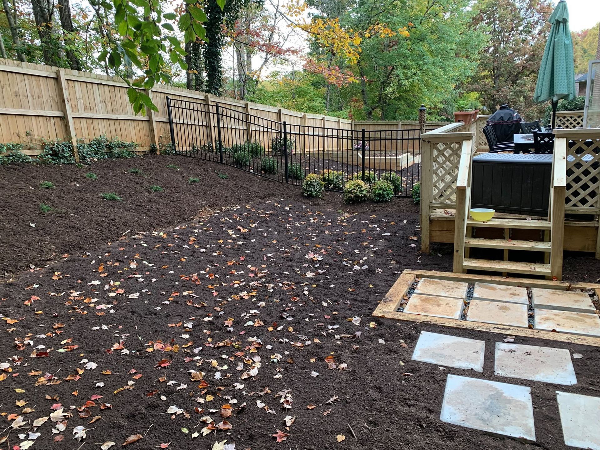 Backyard with freshly tilled soil, fenced perimeter, stone stepping path, and wooden deck stairs