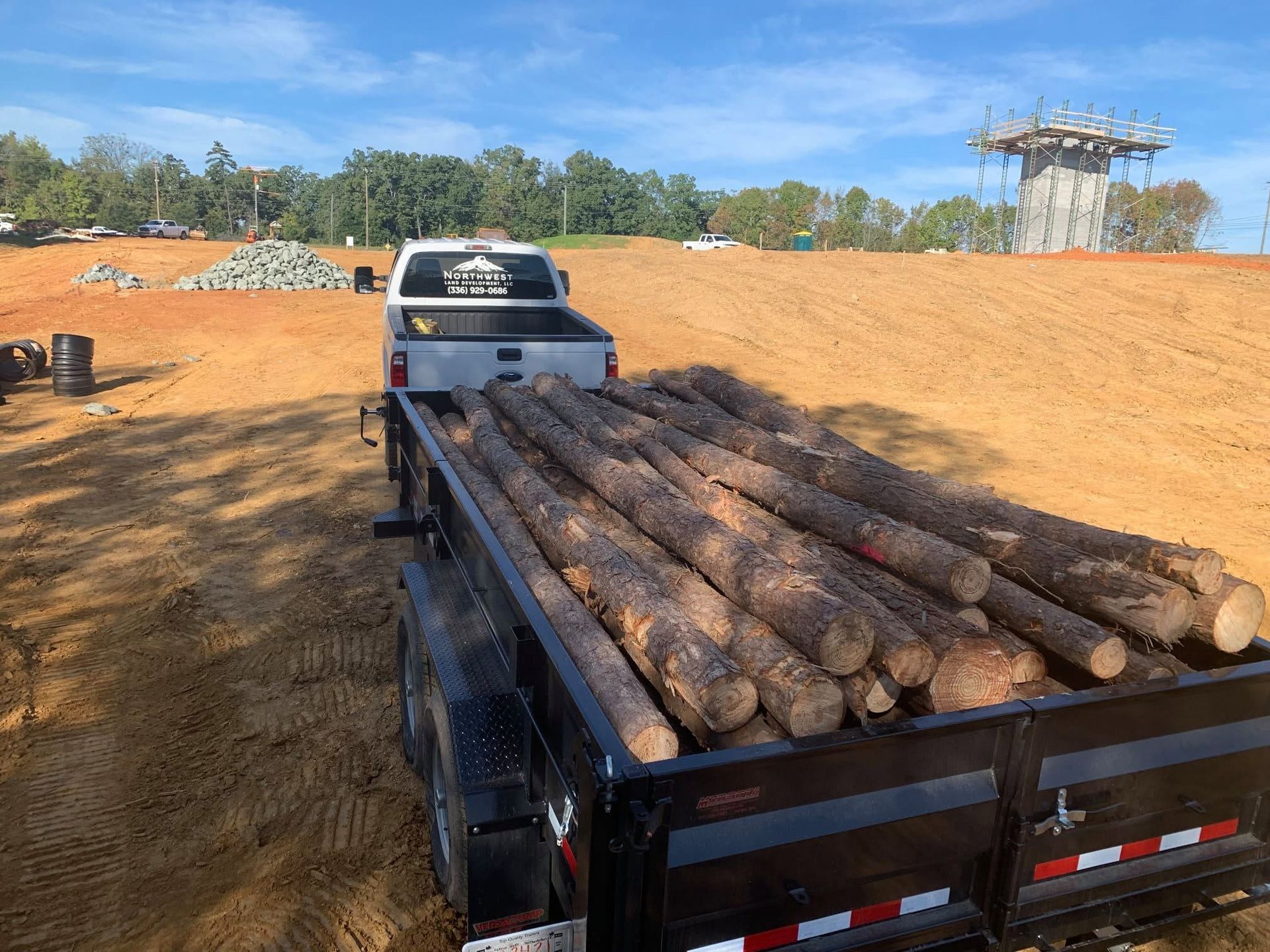 Pickup truck hauling logs on a dirt road at a construction site under a blue sky