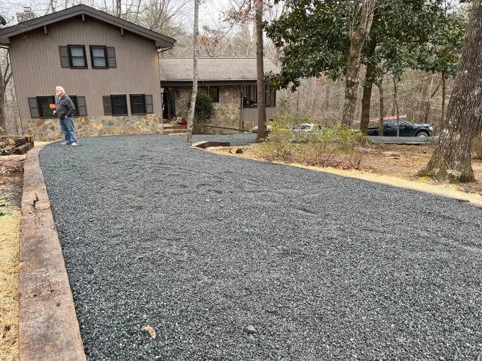Freshly laid gravel driveway leading to a house, with a worker standing near the entrance.