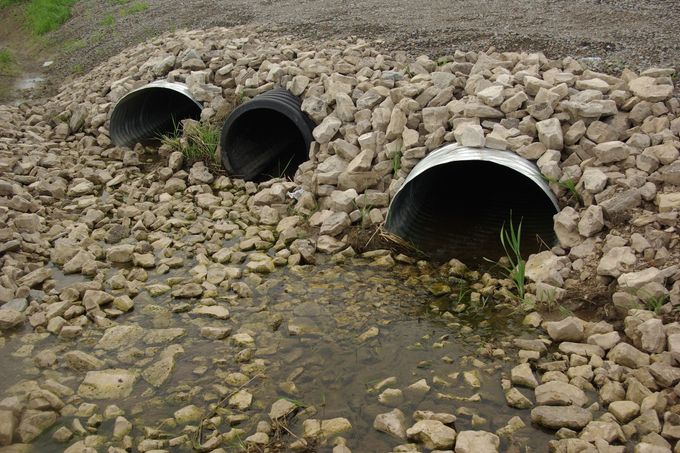 Three drainage pipes in a rocky embankment, with water flowing from the center pipe.