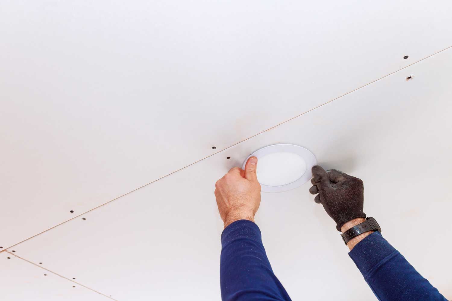 Person, der installerer en indbygget lampe i et hvidt loft.
