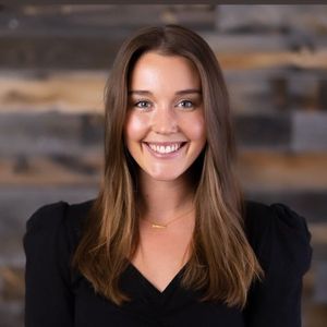 A woman in a black shirt is smiling in front of a wooden wall.