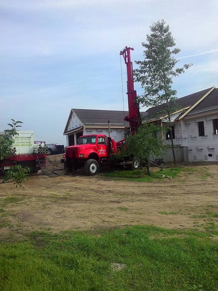 Red well drilling truck next to a house under construction; a tree is nearby.