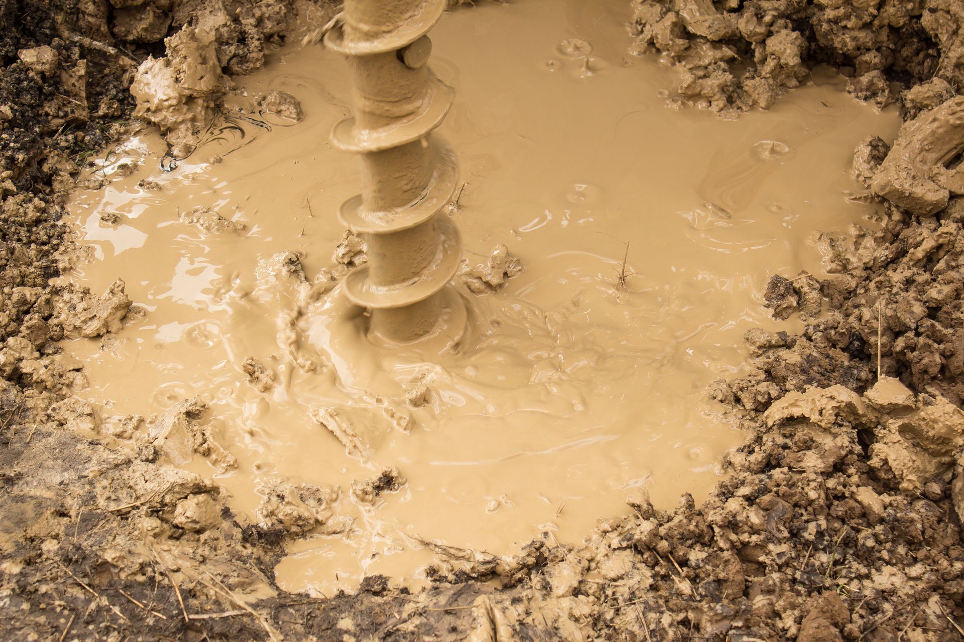Close-up of an auger drill churning muddy soil during ground drilling work.