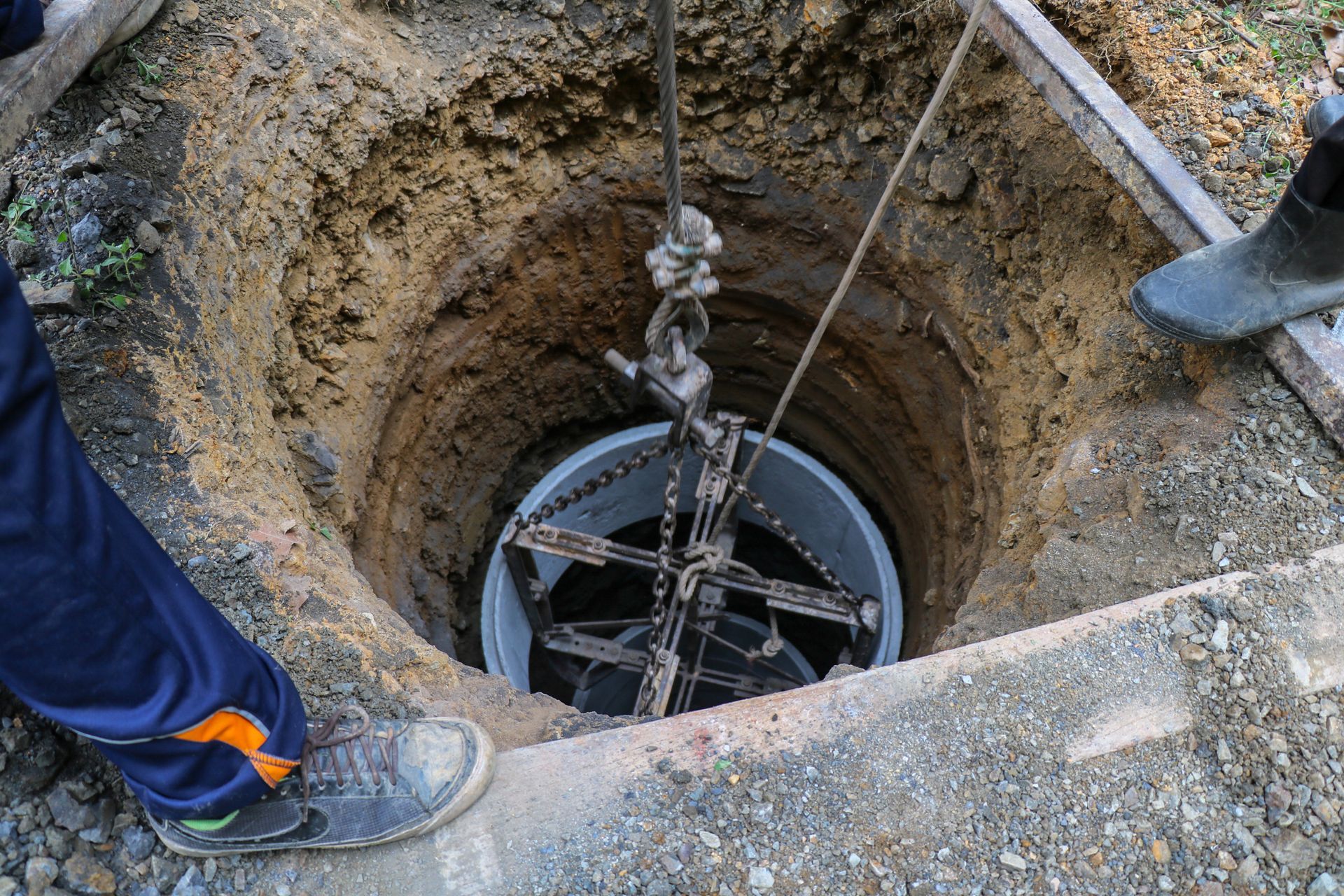 Workers lowering a large metal structure into a deep, circular hole in the ground.