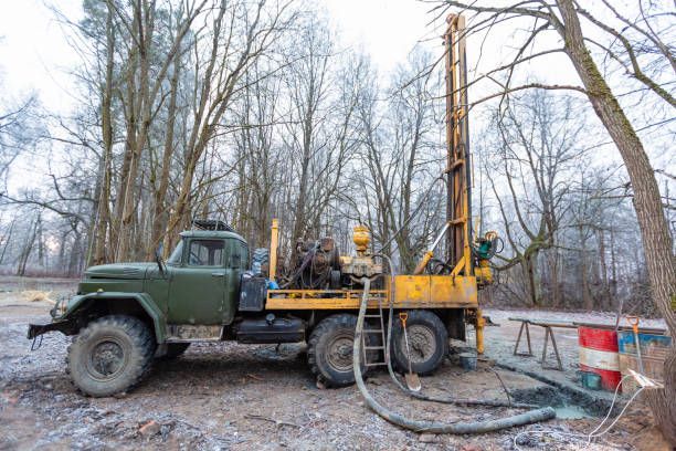 Green drilling rig on a truck, drilling water well in a wooded area.