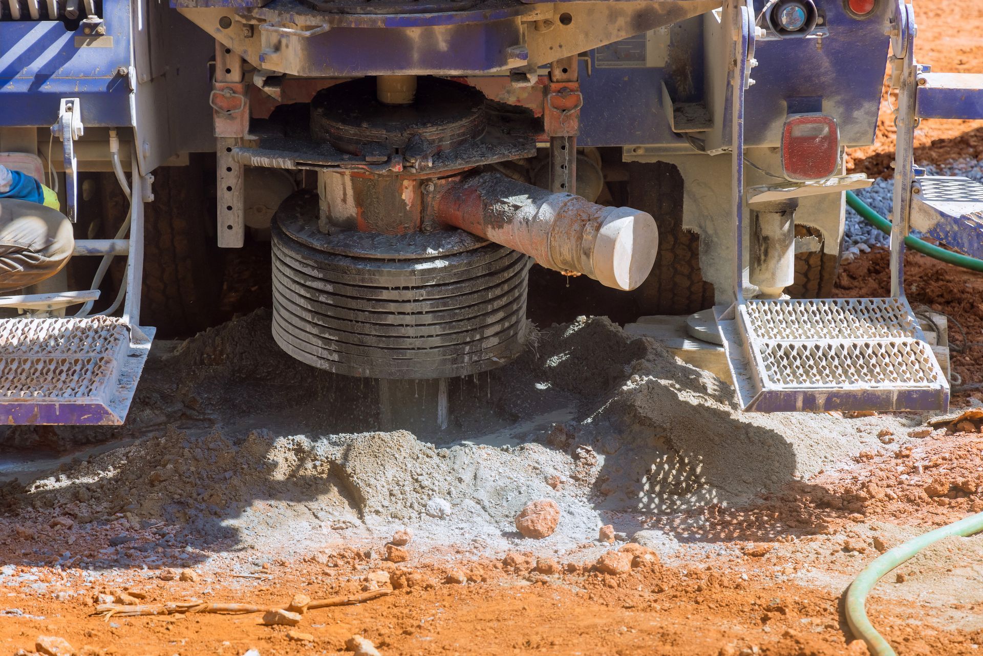 Drilling rig operating, spewing soil and water onto reddish-brown ground.
