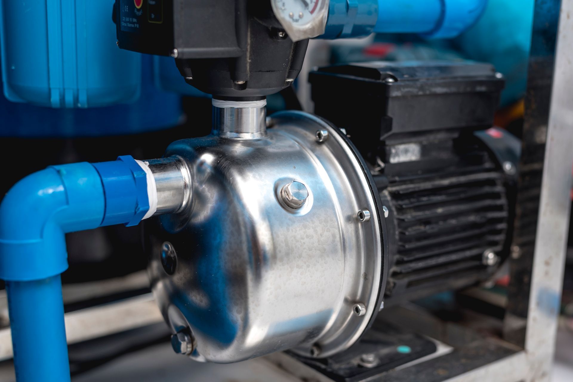 Close-up of a shiny, stainless steel water pump with blue pipes attached and a black motor.