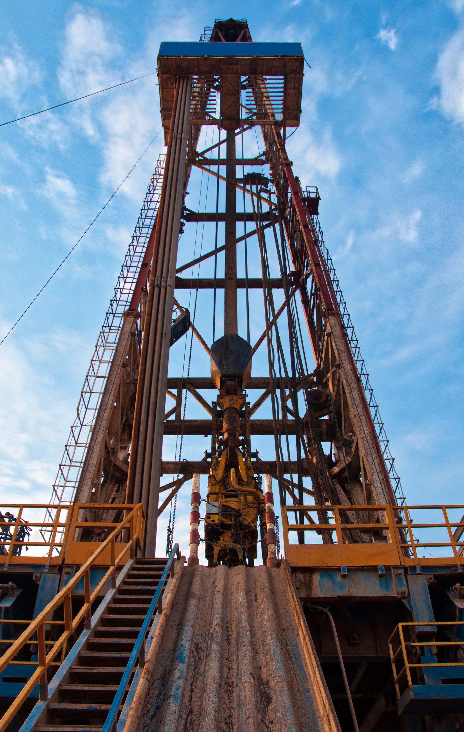 Drilling rig against a blue sky, with metal framework and stairs.