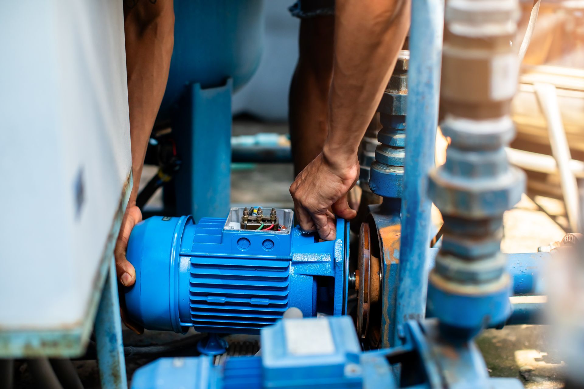 Person's hands working on a blue water pump, outdoors.