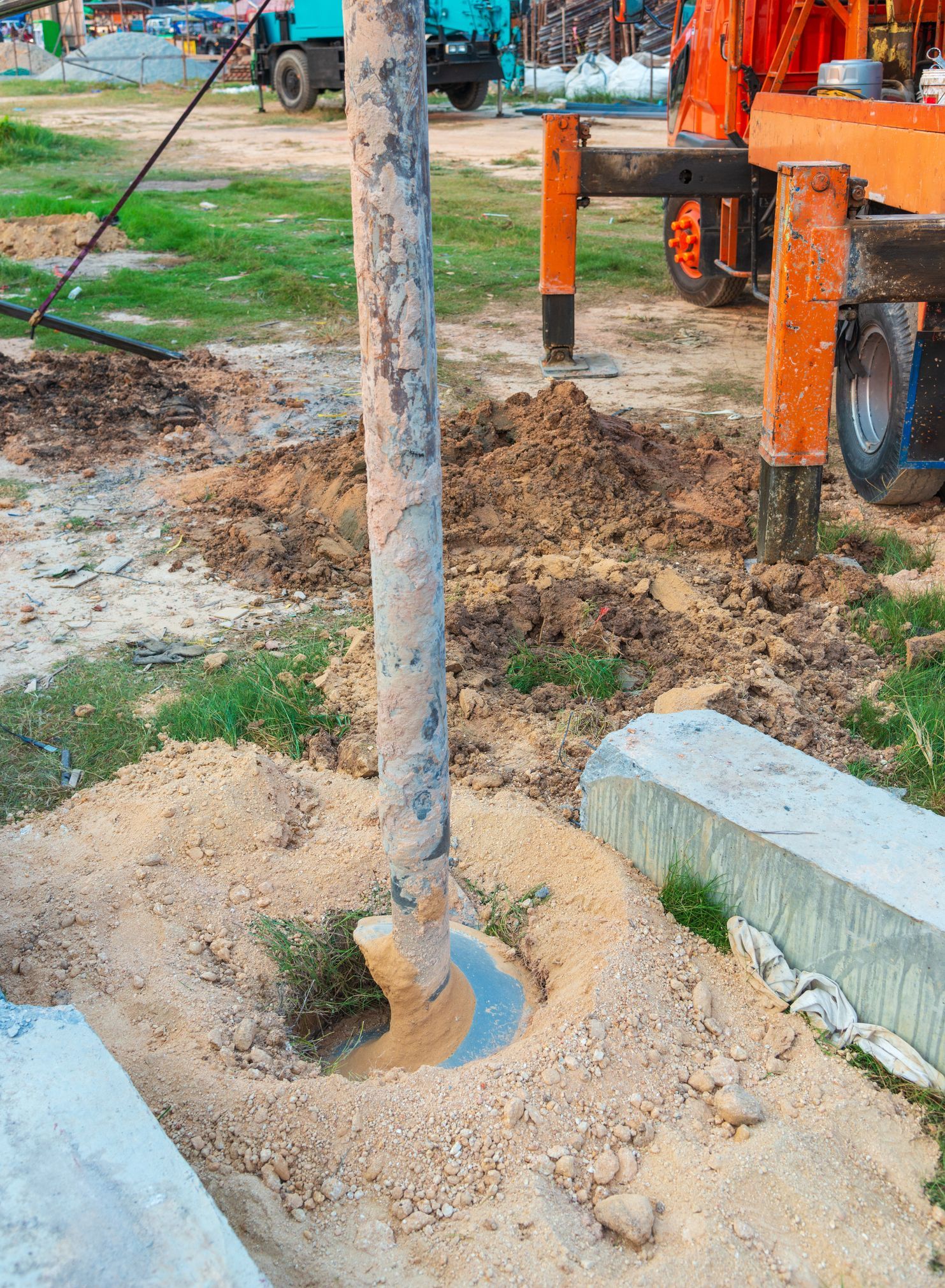 A water well drilling site with heavy equipment and soil excavation in progress on a clear day.