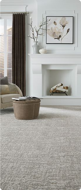 Cozy living room with white fireplace, framed wall art, wicker basket, and neutral sofa beside tall curtains.