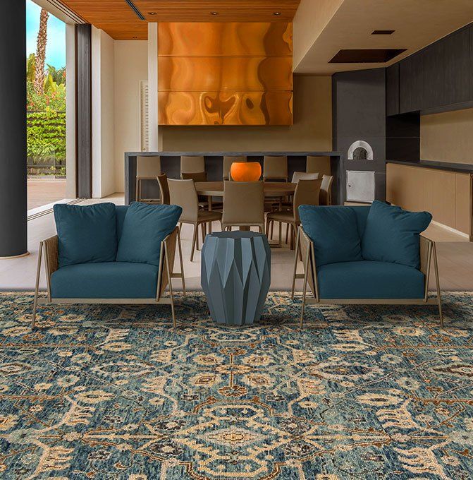 Modern living room with teal armchairs, patterned rug, and open kitchen area