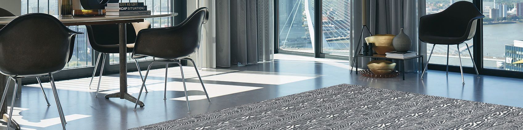 Modern lobby with tables, black chairs, large windows, and sunlight on a patterned carpet.