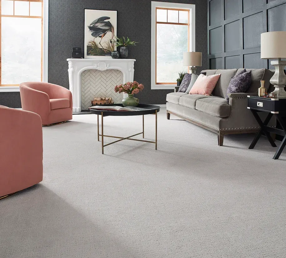 Elegant living room with gray sofa, pink chair, black coffee table, and white fireplace
