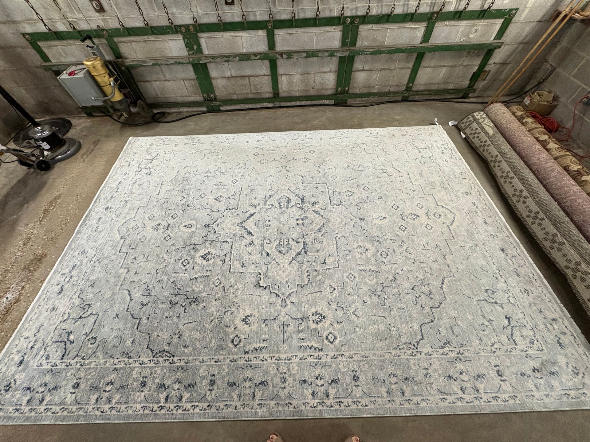 Large pale patterned rug laid out in an industrial workshop with shelves and equipment around it