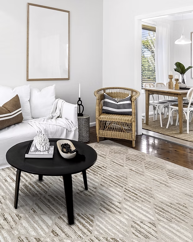 Bright living room with white sofa, black coffee table, wicker chair, and dining area beyond glass doors