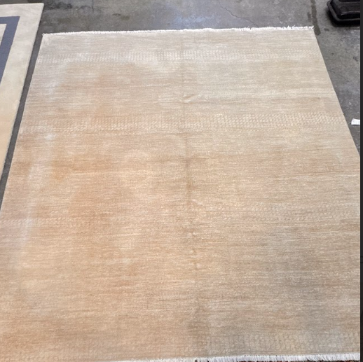 Beige rectangular rug laid flat on a gray floor, with a white border around the edges
