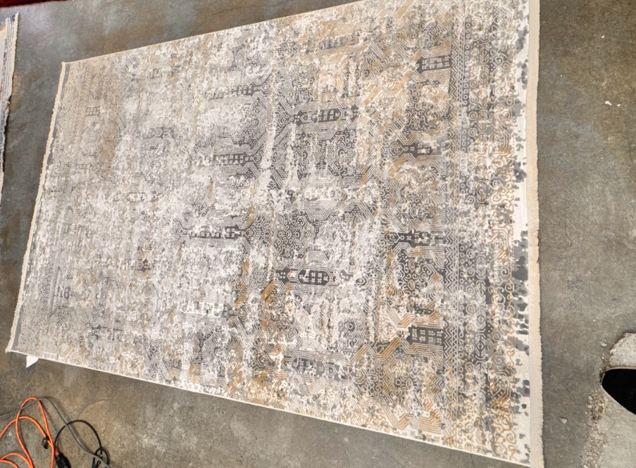Weathered rectangular rug or mat with faded gray and beige patterns lying on concrete floor