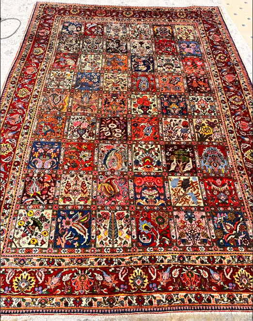 Colorful patterned rug with a red border, featuring intricate floral and geometric designs.