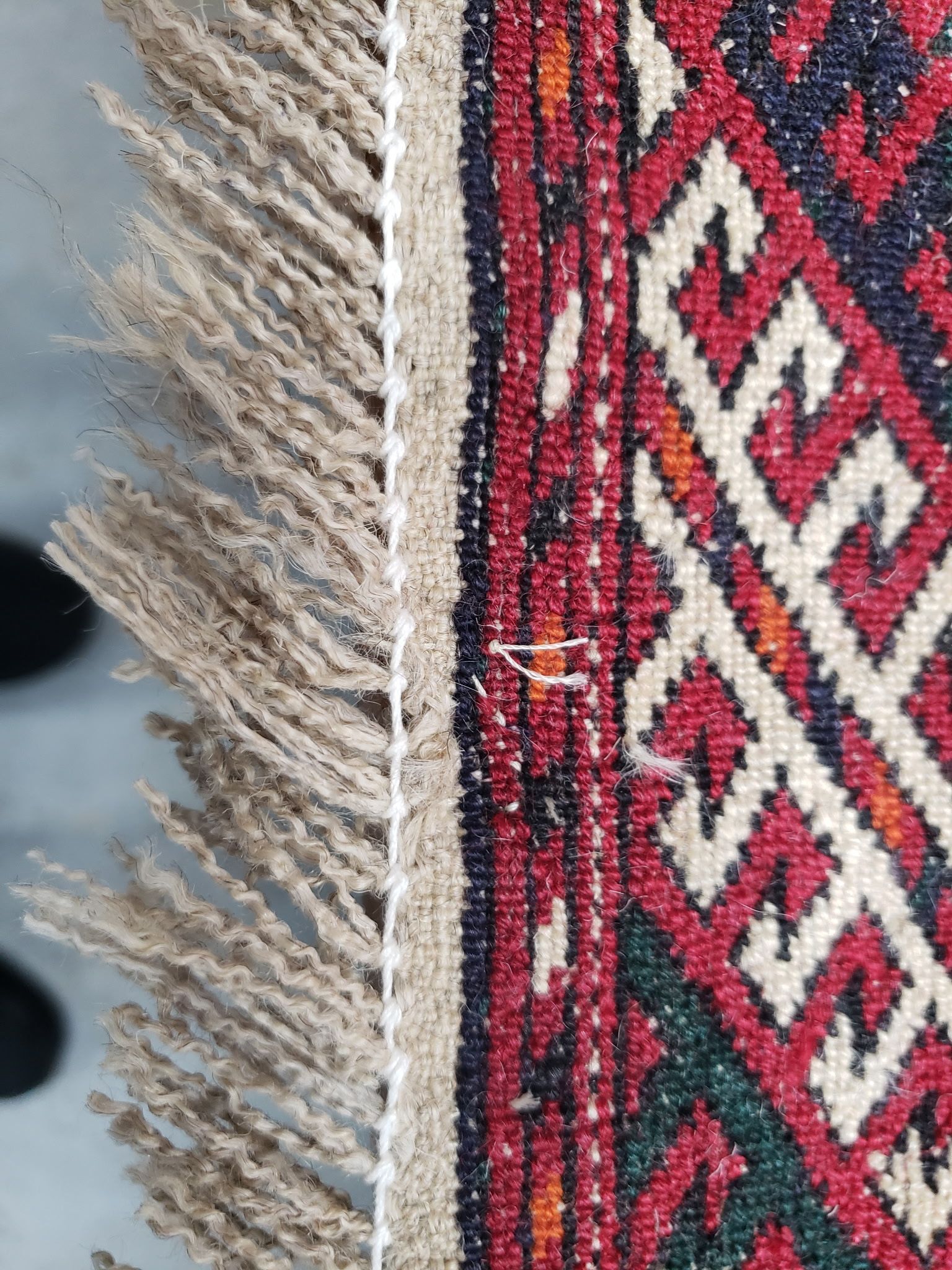 Close-up of a patterned red, white, and green woven rug with beige fringe on the edge