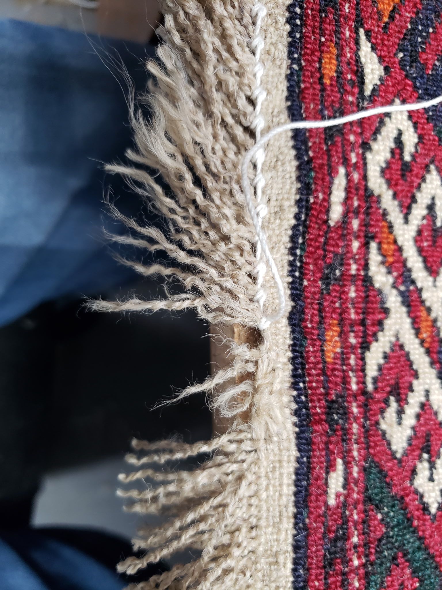 Close-up of a frayed beige carpet edge beside a red patterned rug with a white thread visible