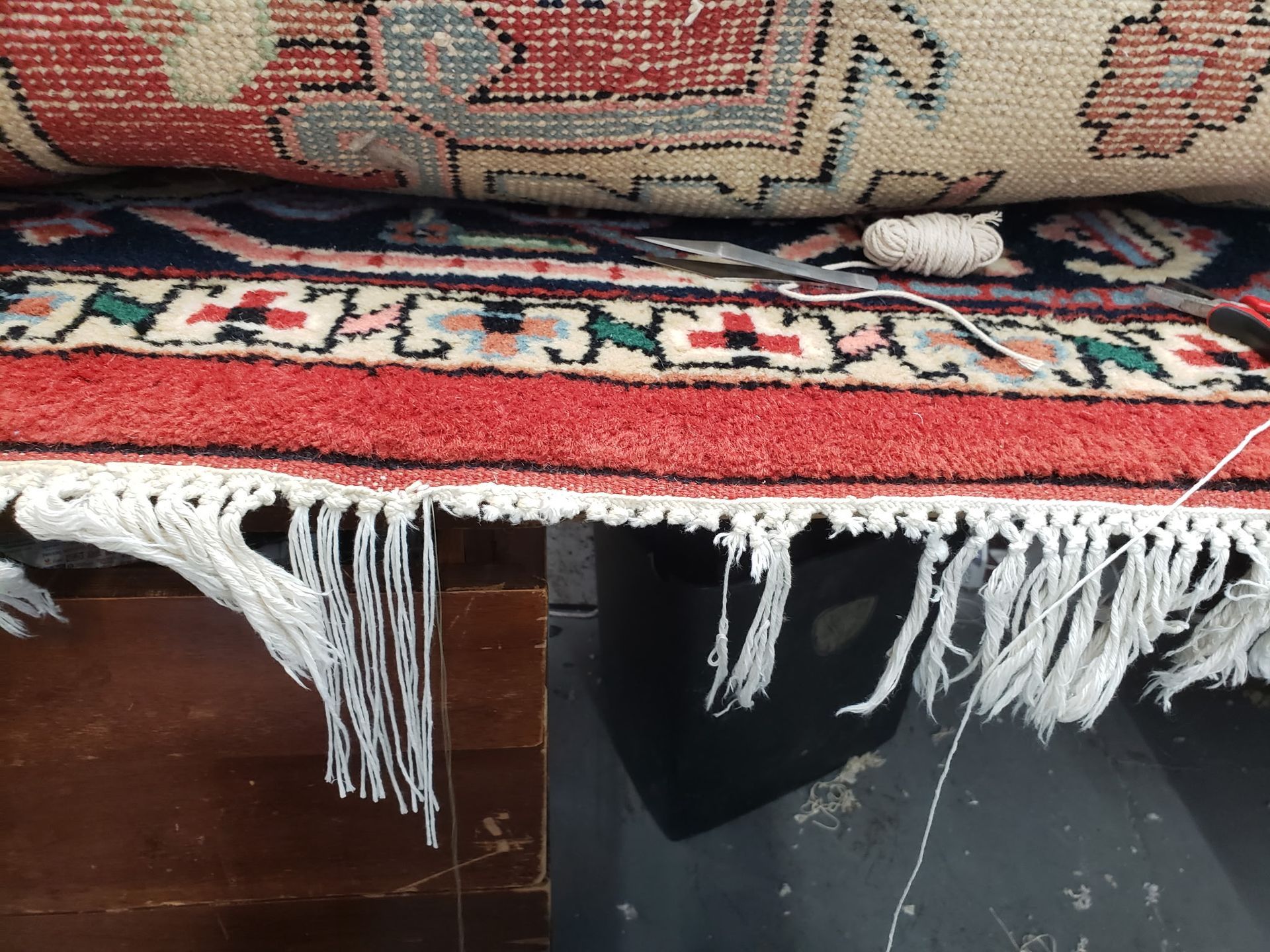 Red patterned rug draped over a dark wooden surface with white fringe hanging down
