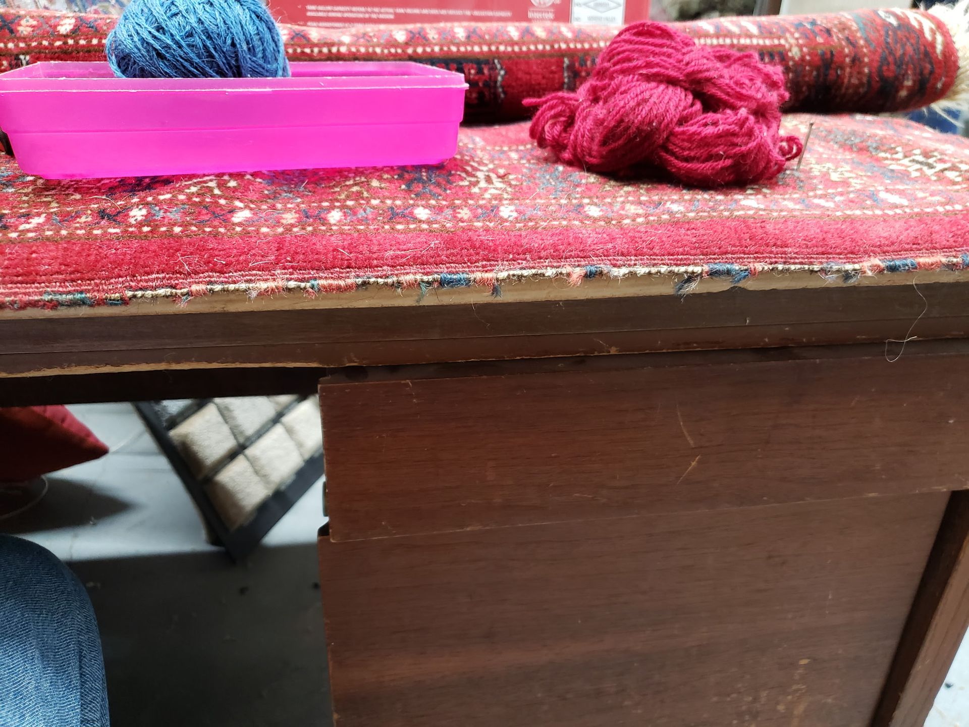Pink tray with blue yarn and red yarn balls on a patterned table over a wooden cabinet