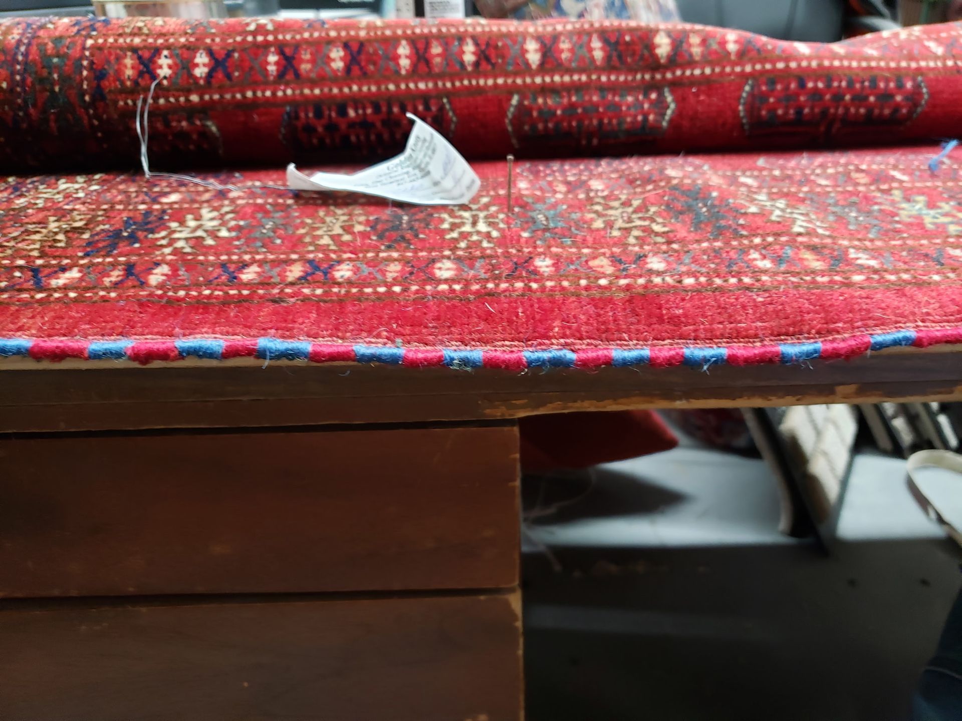 Red patterned fabric rolled over a wooden surface with a small gray paper item on top