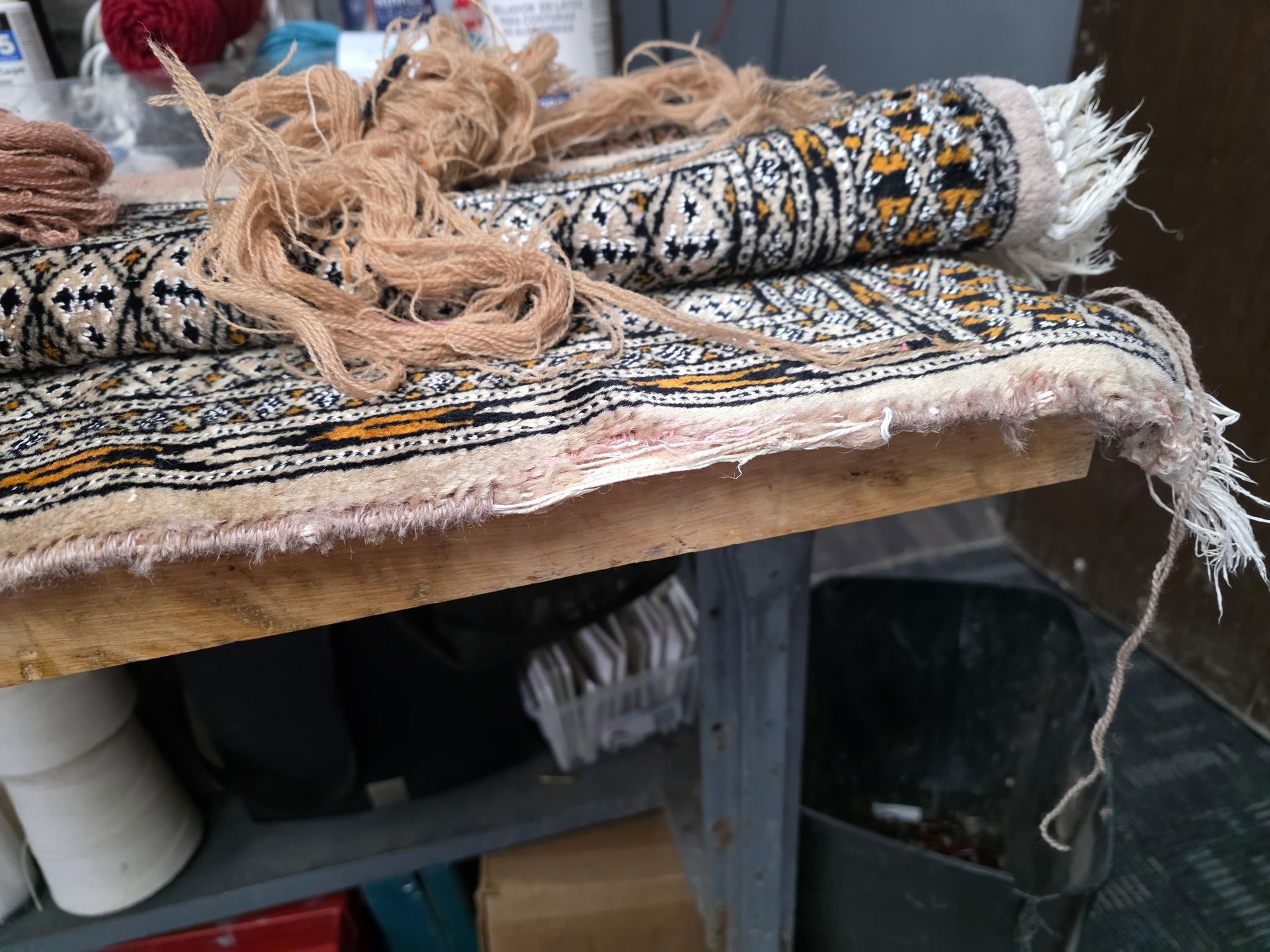 Rolled woven textiles on a worktable in a craft workshop, with frayed edges and beige fibers.