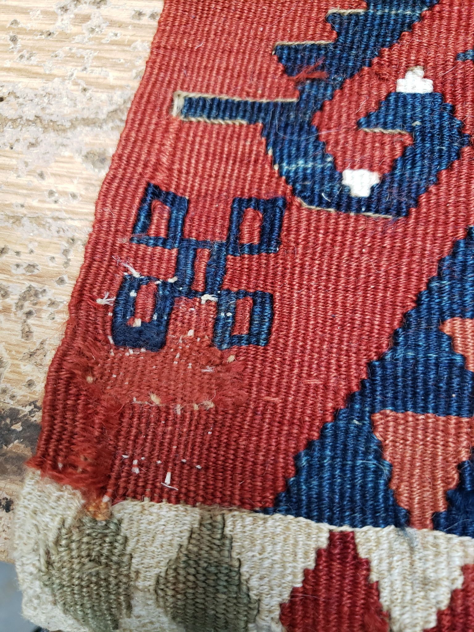 Close-up of a red and blue patterned woven textile with geometric shapes and fringe edge