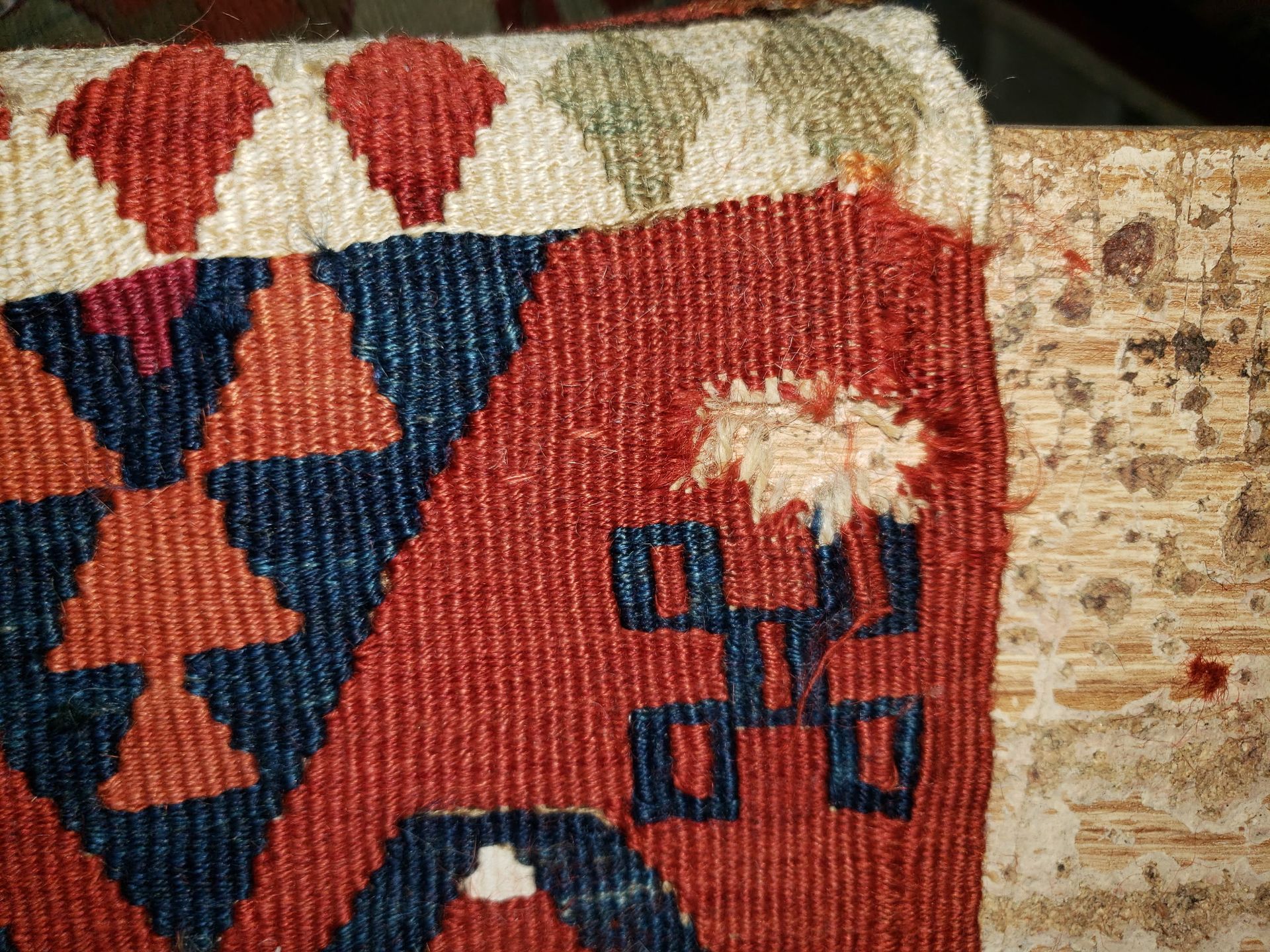 Close-up of a red woven textile with blue geometric patterns and a cream fringe on a wooden surface