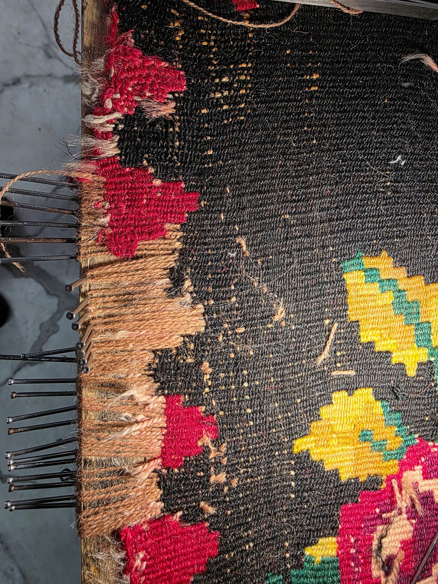 Frayed woven rug edge with black, red, yellow, and beige pattern on a gray floor