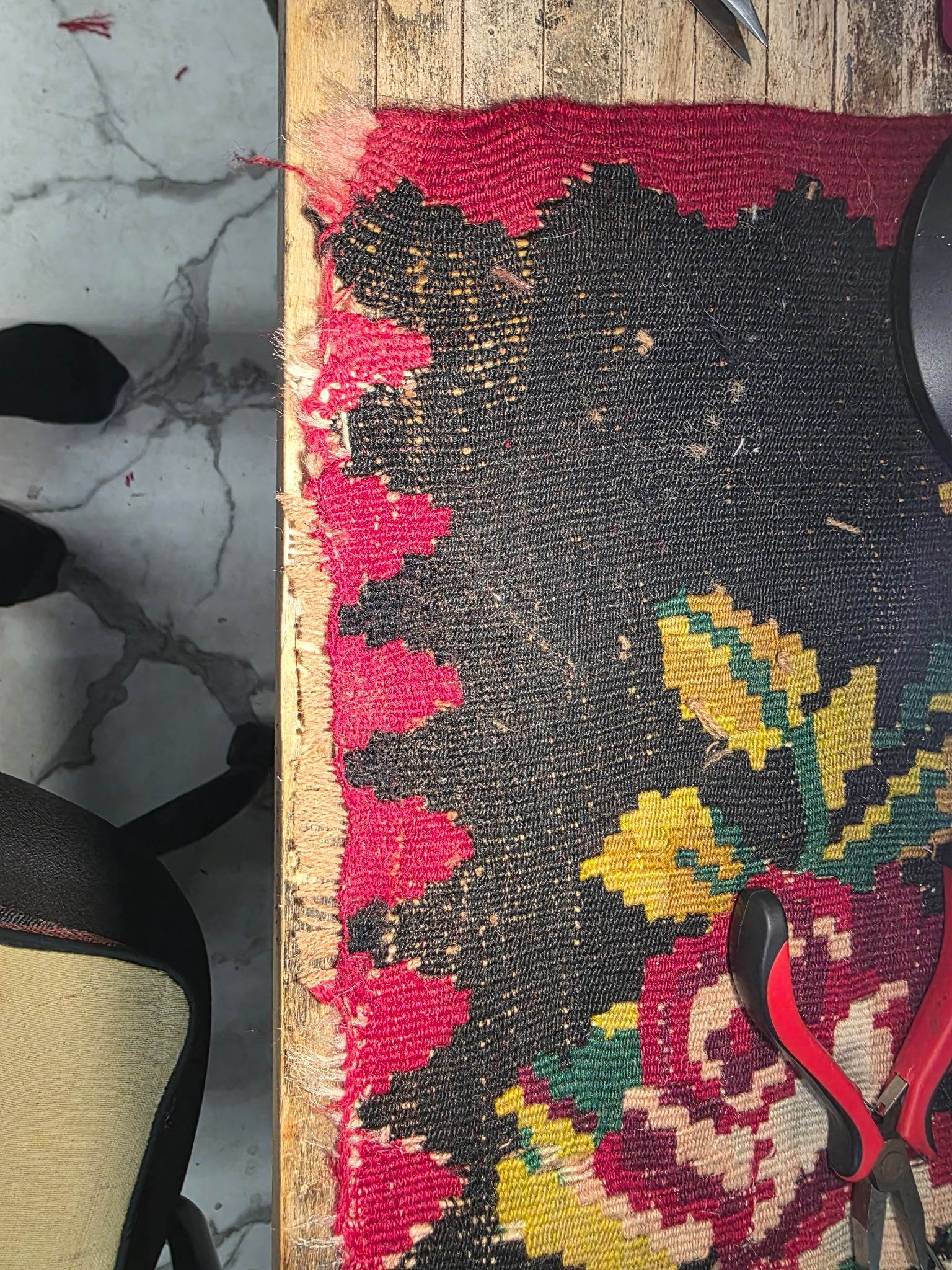 Weathered floral rug beside cracked concrete wall with black containers on the left