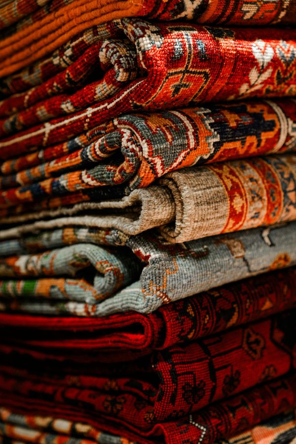 Stacked rolled rugs in red, orange, and gray patterned textiles with ornate designs