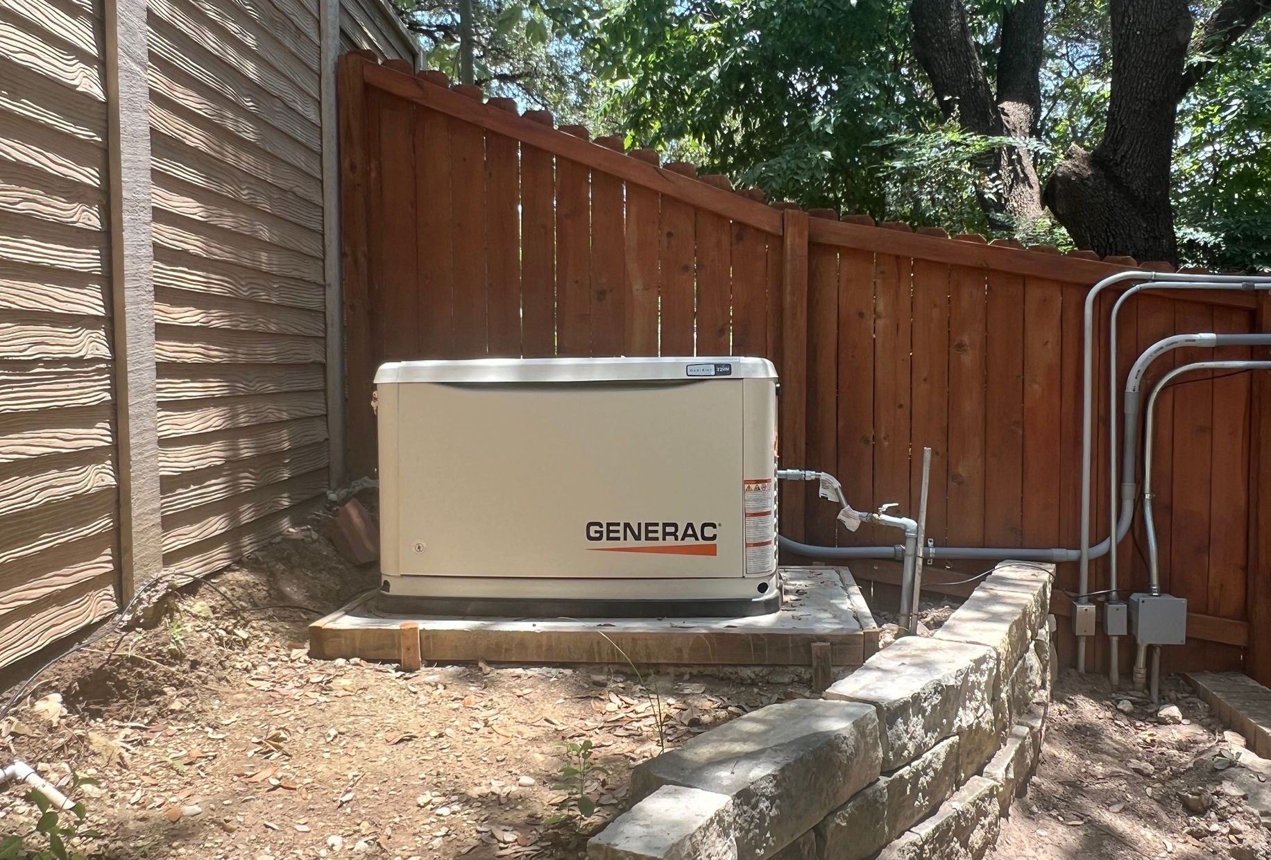 A Generac home generator is mounted on a concrete slab near a wooden fence.
