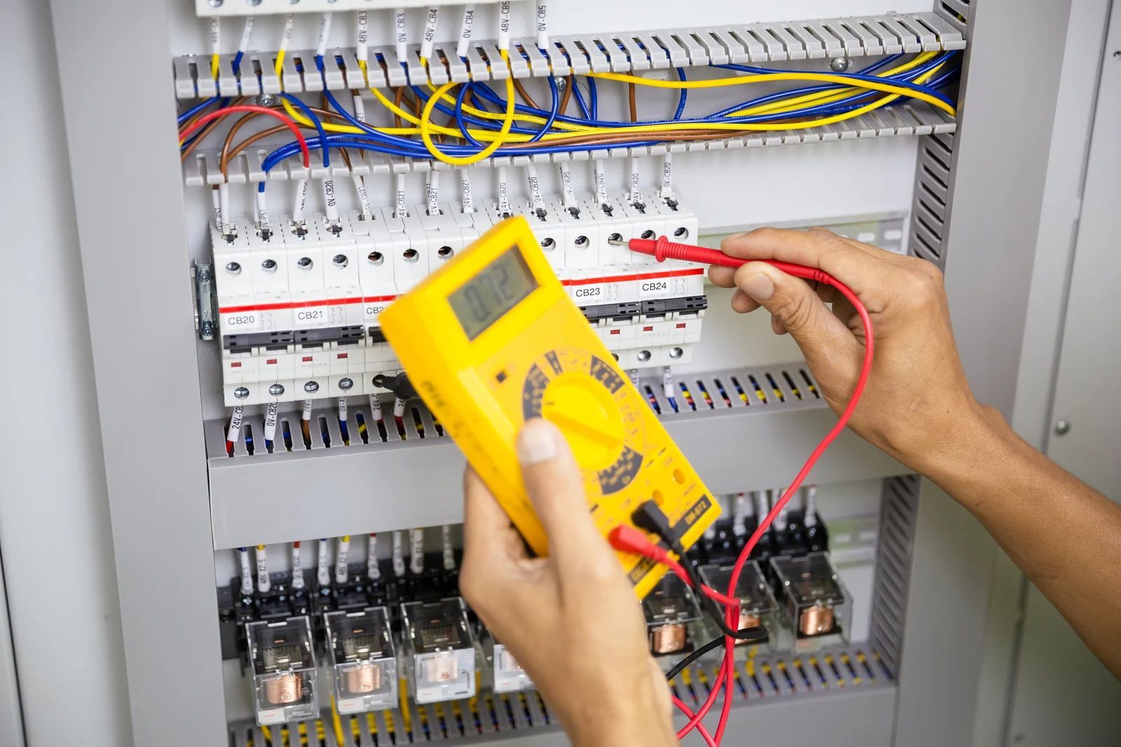 Technician testing an electrical control panel with a yellow multimeter and red probes