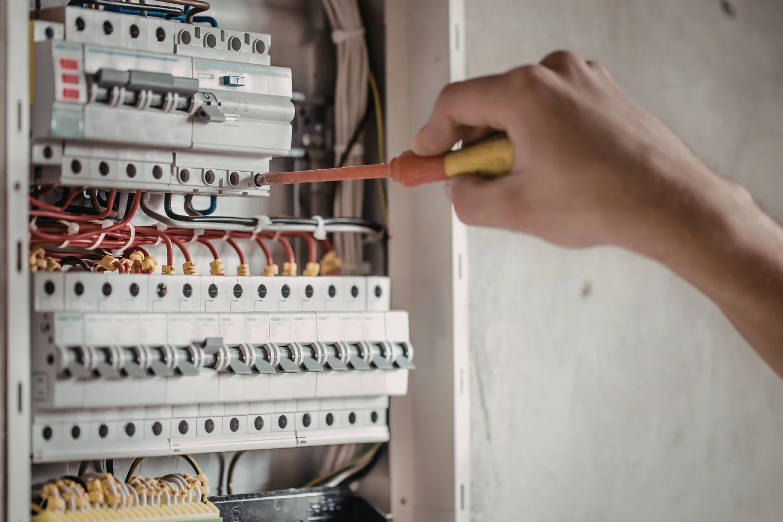 Hand using a screwdriver to work on an electrical circuit breaker panel with exposed wiring