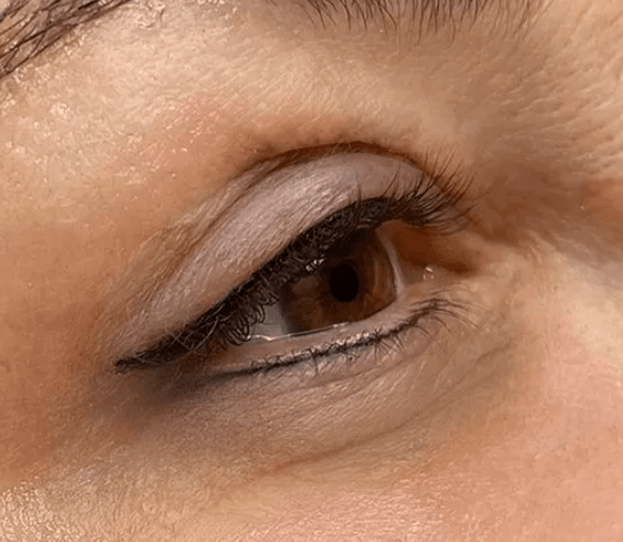 Nahaufnahme eines menschlichen Auges mit dunklem, semi-permanentem Eyeliner, der entlang des oberen und unteren Wimpernkranzes tätowiert wurde.