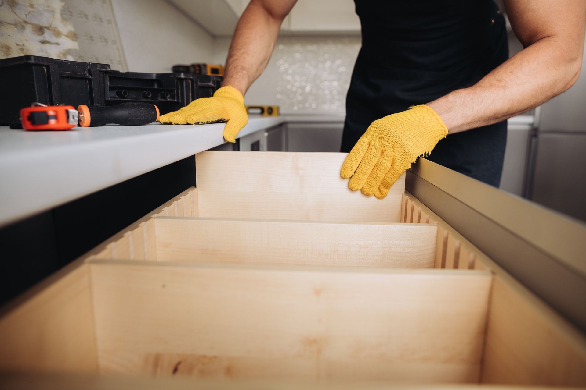 Person installing wooden drawer slides in a kitchen cabinet, wearing yellow gloves.