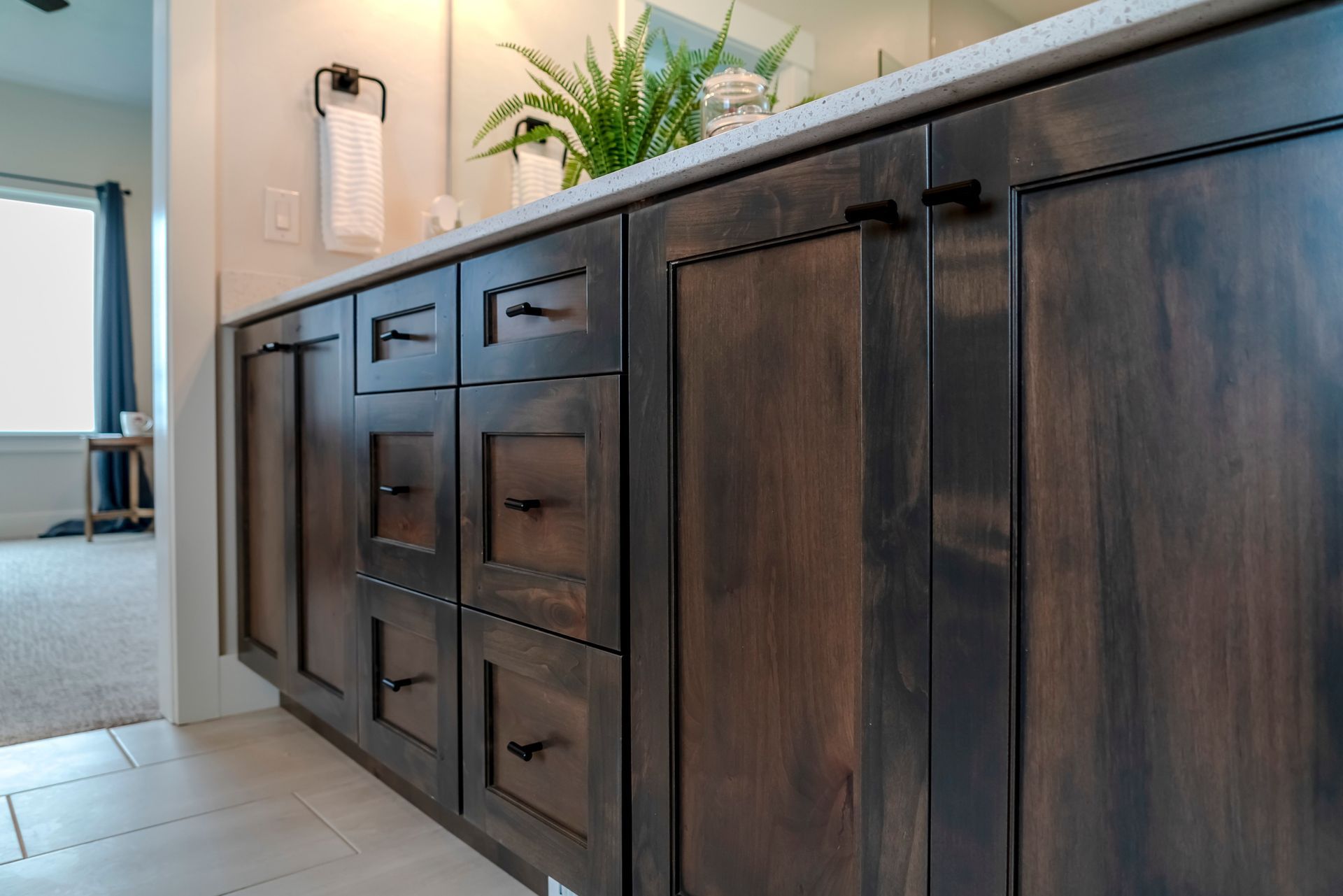 Dark wood bathroom vanity with drawers and cabinet doors beside a sink and potted plant