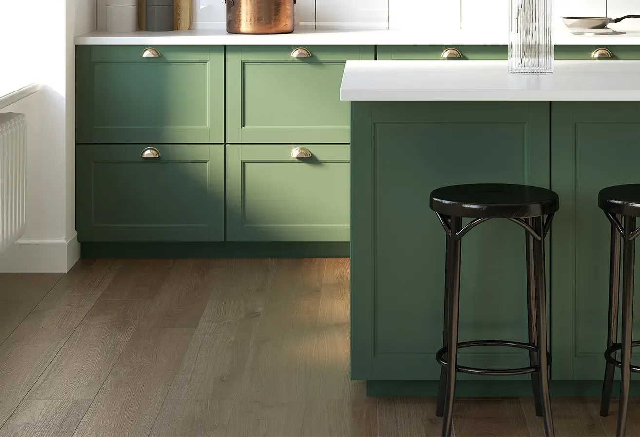 Green kitchen cabinets and island with black stool on wood floor, lit by daylight