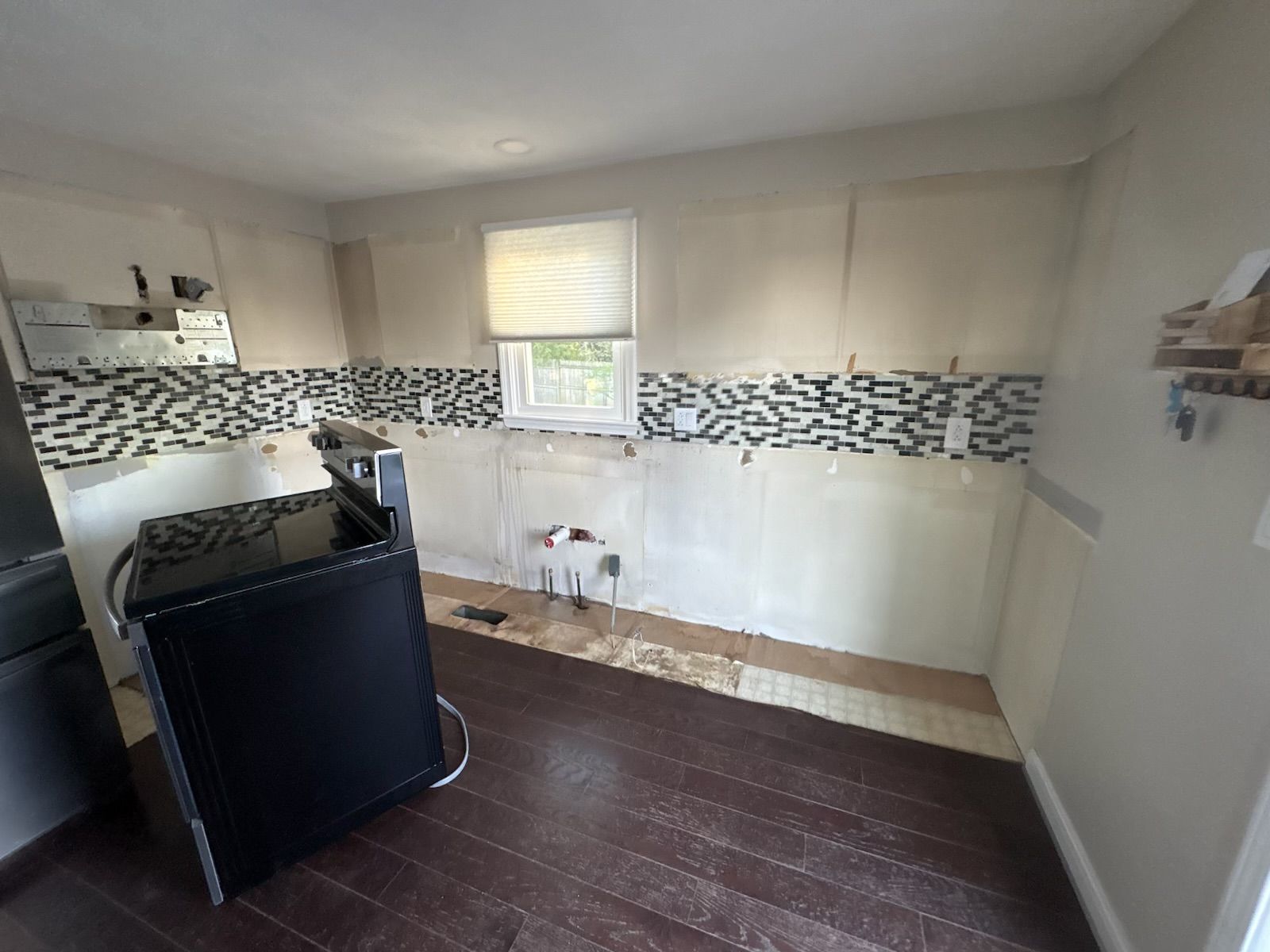 Empty kitchen under renovation with white walls, mosaic backsplash, and dark wood flooring
