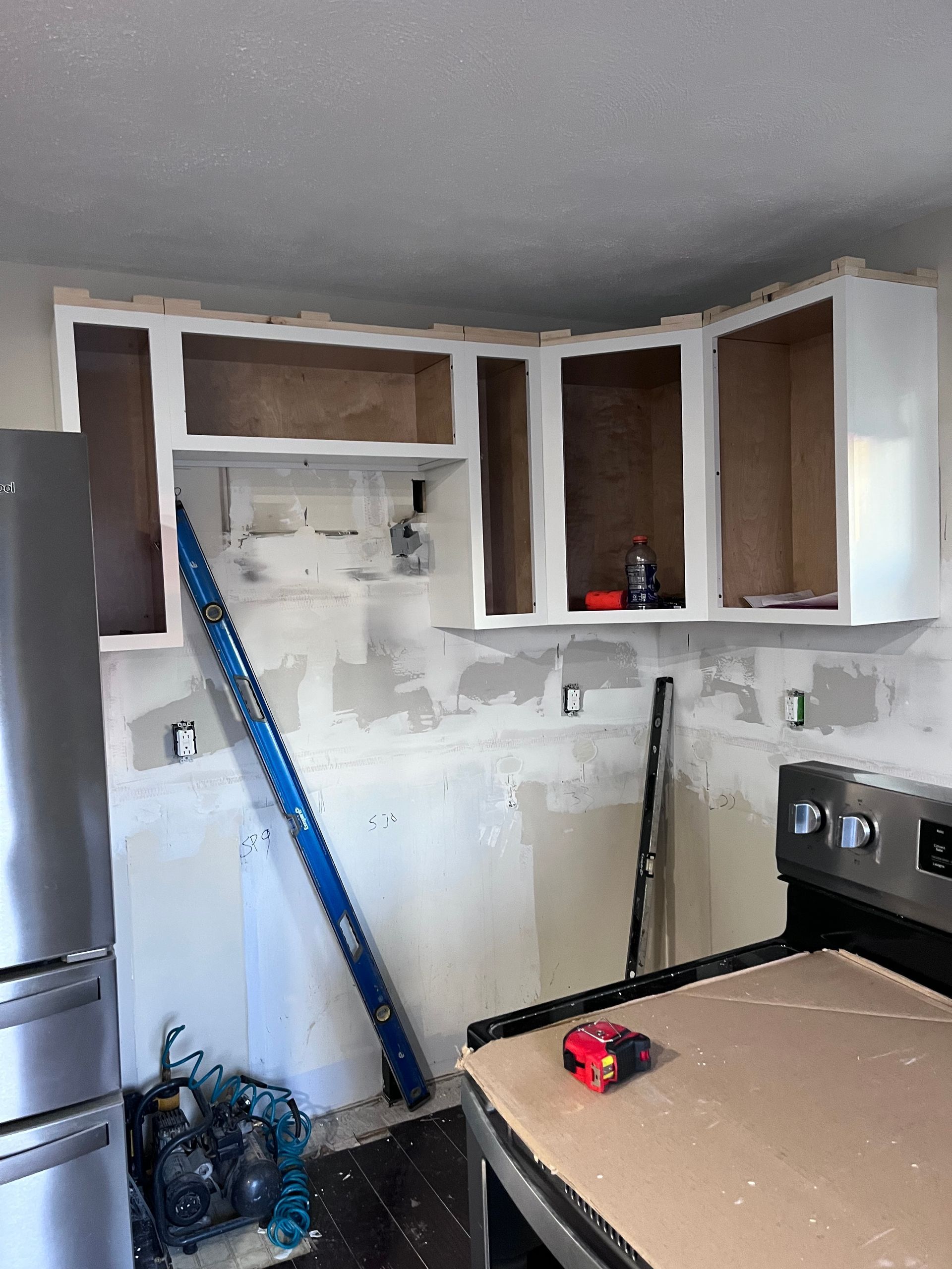 Partially remodeled kitchen with exposed cabinets, white walls, and tools on the counter